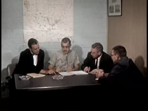 Four men seated at a conference table lean in to review documents together.
