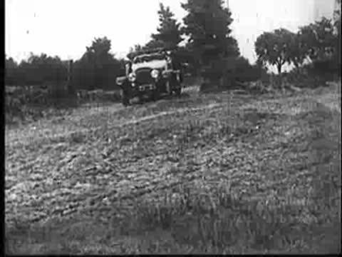 Vintage open-top car driving along a dirt road in the countryside.