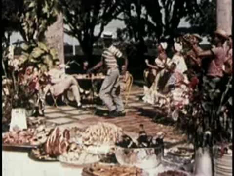 Outdoor gathering with people dining and traditional dancers performing nearby.