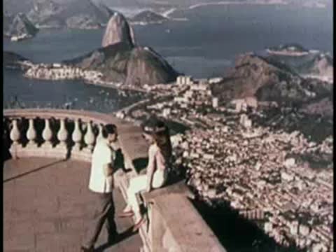 Couple sitting on a stone wall overlooking a coastal city and harbor.