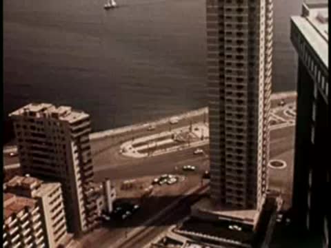 Aerial view of a modern skyscraper and coastal road with vintage cars.