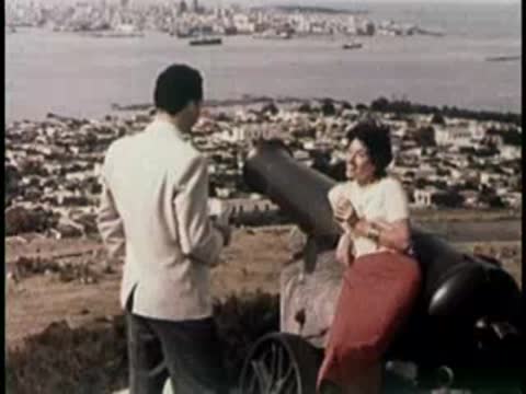 Man and woman talking by a large historic cannon overlooking town.