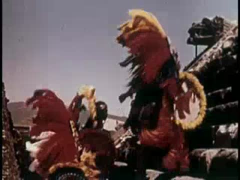 Dancers in elaborate feathered costumes performing near ancient ruins.