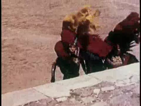Costumed dancers moving near a stone wall outdoors.