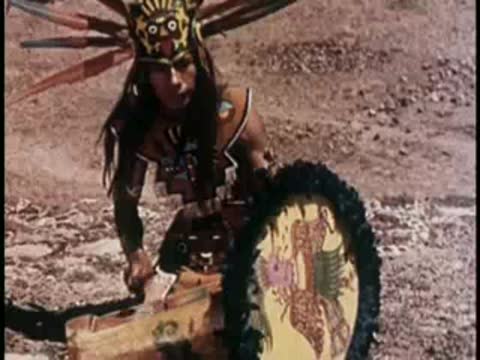 Close-up of a drummer playing a large decorated drum in traditional attire.
