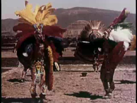 Traditional dancers in elaborate feathered headdresses performing outdoors.