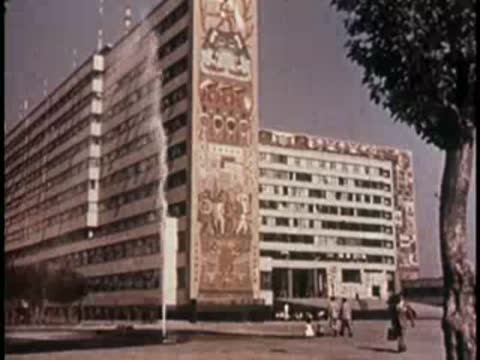 Modern multi-story building with mural and tree in foreground.
