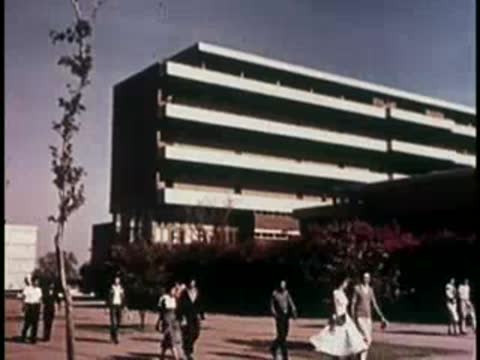 Modern building exterior with people walking on a paved plaza.
