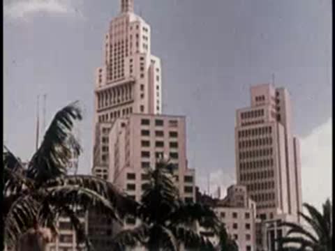 Tall vintage skyscrapers and palm trees under a daytime cloudy sky.