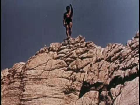 A person standing on a rocky cliff overlooking the sea, 1950s style.
