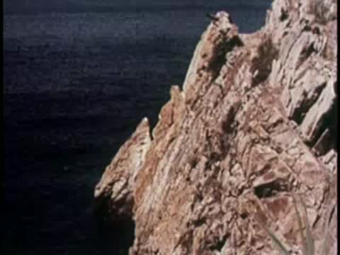 A person diving from a rocky cliff into the sea, 1950s.