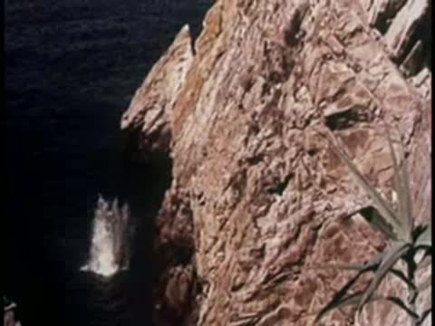 A person splashing into the sea from a rocky cliff, 1950s.