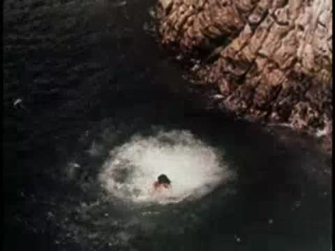A person swimming in the sea near rocky cliffs, 1950s.