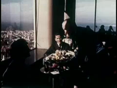 A waiter serving food to people dining in a restaurant with large windows.