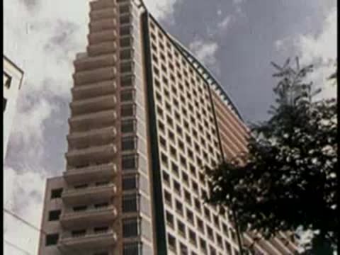 Low-angle shot of a tall curved skyscraper with balconies against clouds.