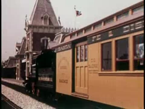 A steam train pulling into a station with a vintage building, 1950s.