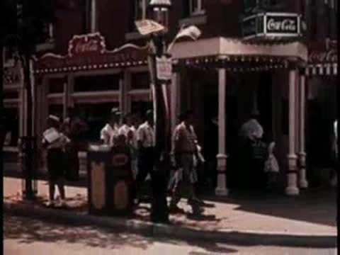 People walking near a storefront with vintage signs, mid-century era.