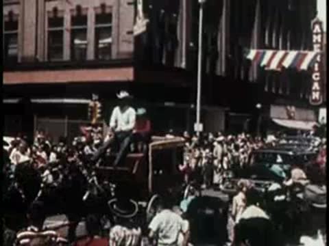 A crowd gathered in a city street watching a parade, mid-century era.