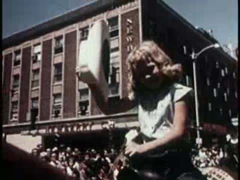 A young girl riding a horse and waving her hat in a parade.