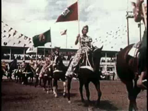 People on horseback carrying flags in an arena, 1950s rodeo.