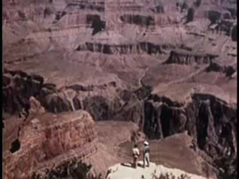 two people standing on a rocky outcrop looking at the grand canyon landscape