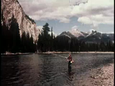 a person standing in a scenic river fishing with a mountain backdrop
