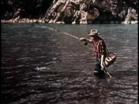 a person standing in a river actively casting a fishing rod and catching fish