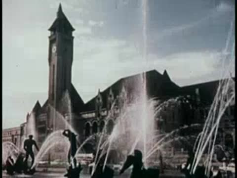 large historic building with a clock tower behind a large decorative water fountain