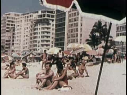 Crowded tropical beach with people relaxing under umbrellas and near water.