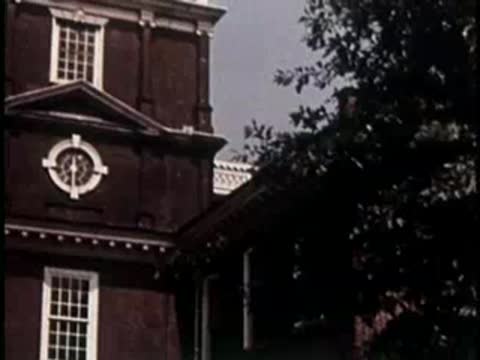 Historic brick building with a tower, trees, and people walking on the grounds.
